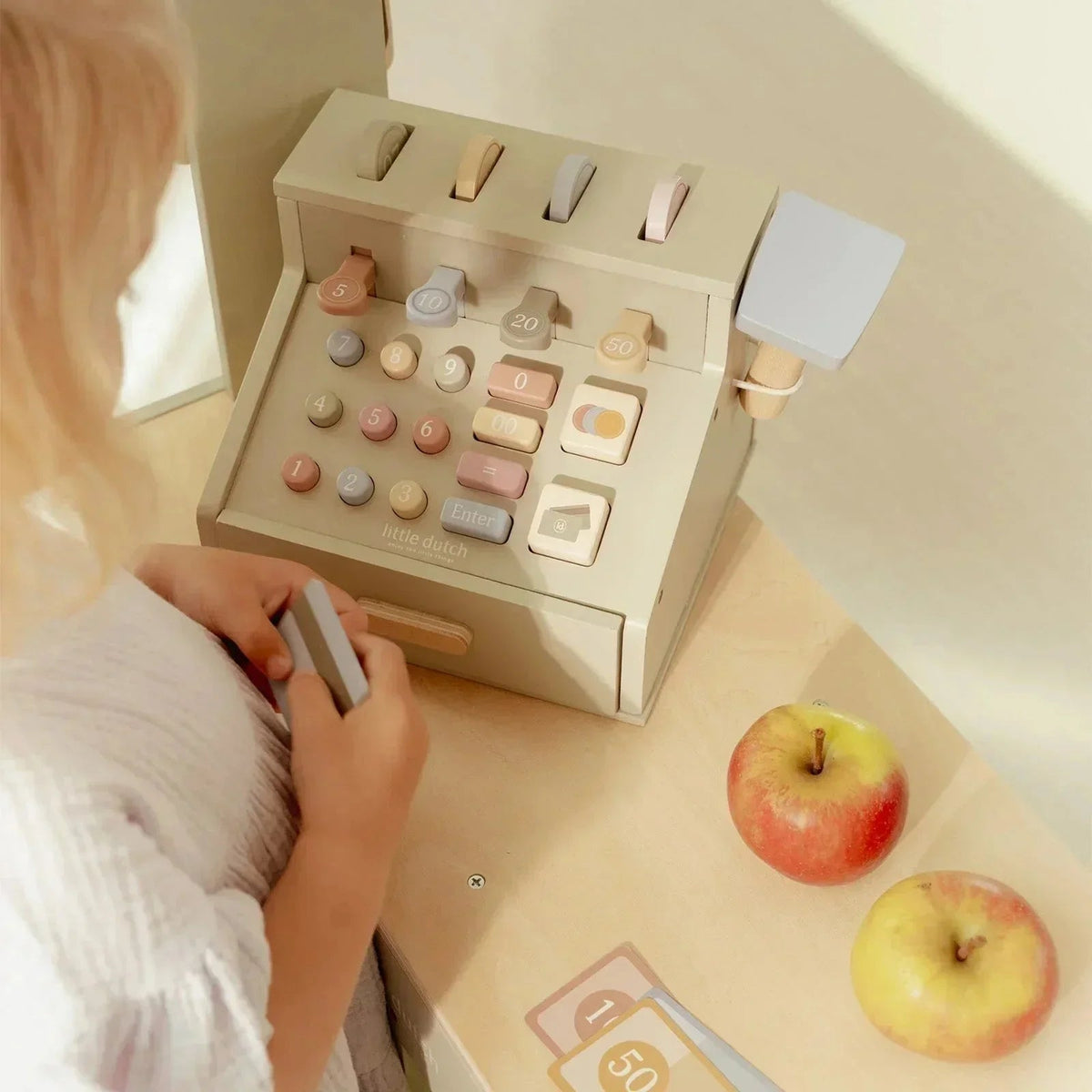 Child playing with a Grayskull Toys wooden cash register and apples on a table.