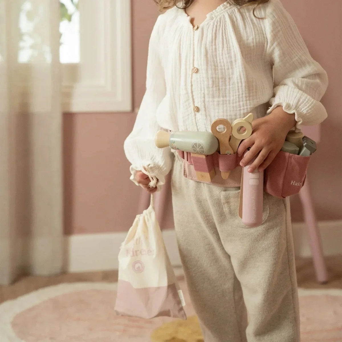 Child wearing a Grayskull Toys Little Dutch hairdresser set tool belt and holding a drawstring bag.