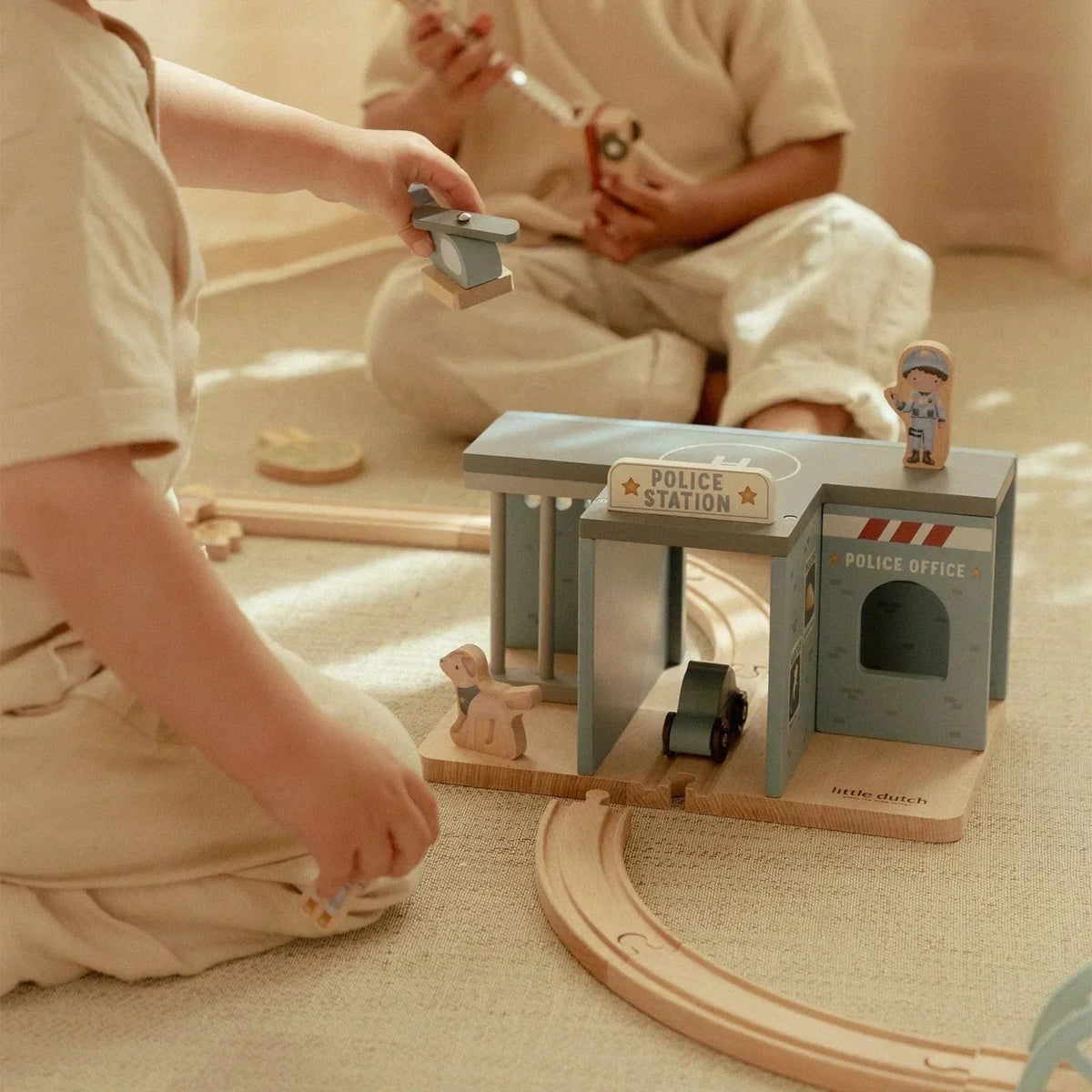 Children playing with Little Dutch Police Station wooden toy set on a floor track.