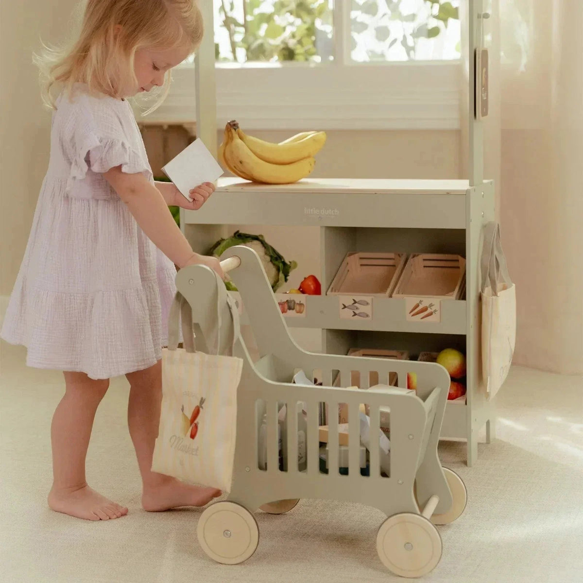 Toddler playing with a Little Dutch wooden shopping cart and toy market stall.