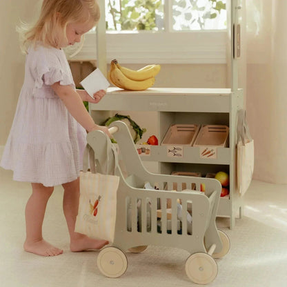 Toddler playing with a Little Dutch wooden shopping cart and toy market stall.