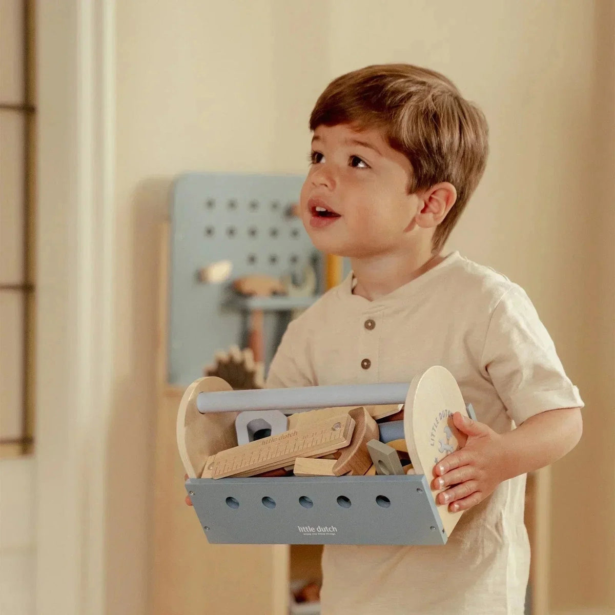 A young child holding a Grayskull Toys wooden toy tool box with various play tools inside.