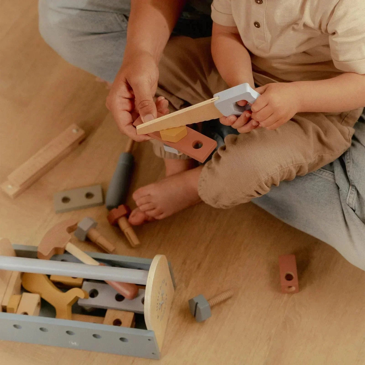 Child and adult playing with Little Dutch Tool Box wooden toy set on a light wooden floor