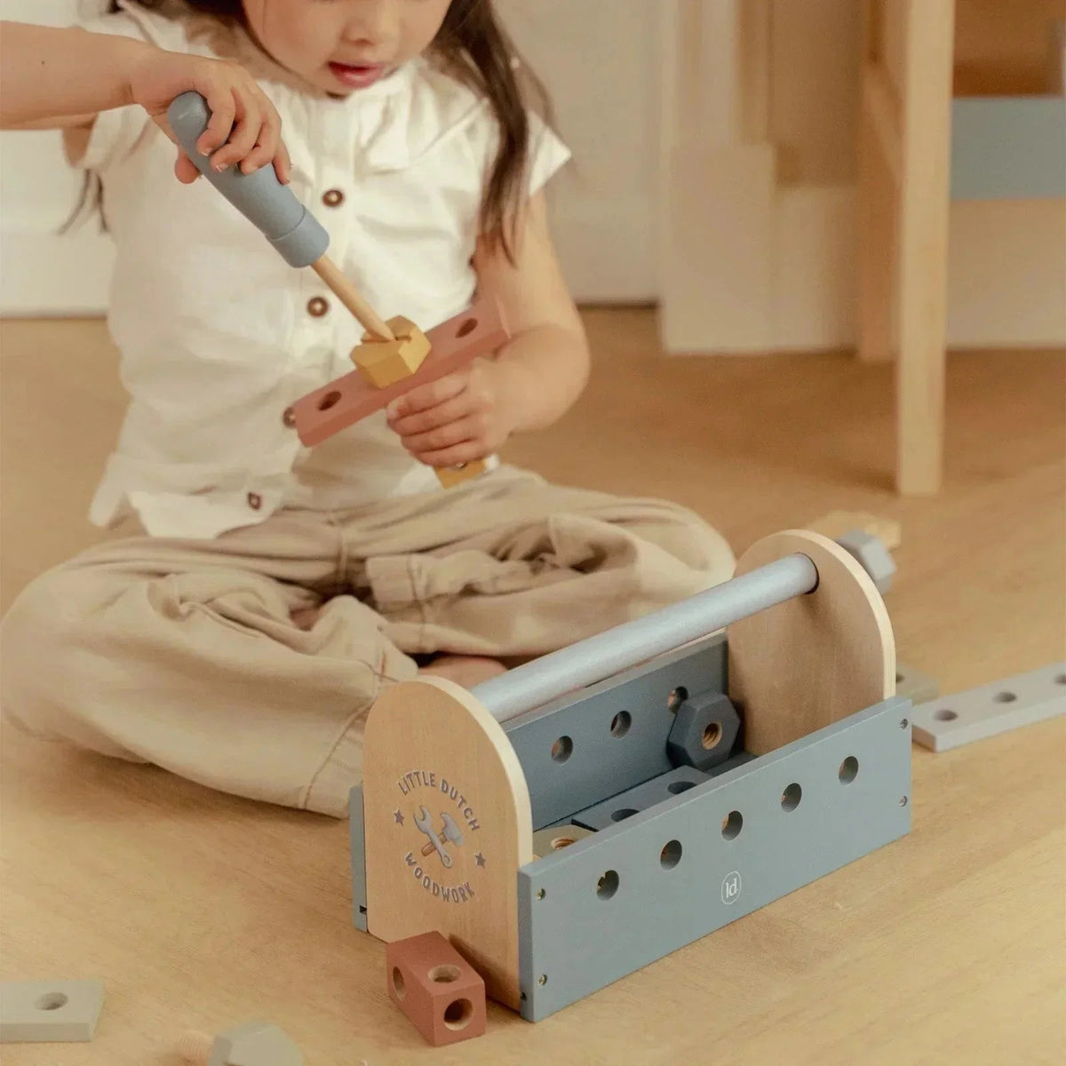 A child playing with the Grayskull Toys Little Dutch wooden tool box set on a floor.